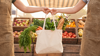 Canvas farmers market tote filled with carrots, greens and fresh bread
