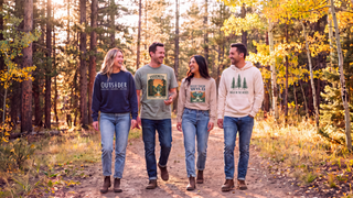 Four friends walking an autumn forest trail at golden hour wearing Artisan Grove apparel: an Outsider crewneck, a Yosemite National Park stamp tee, a Keep Them Wild long sleeve and a Walk in the Woods hoodie.