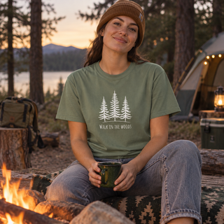 Young woman wearing a Walk in the Woods graphic T-shirt beside a campfire