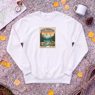 White Rocky Mountain National Park sweatshirt with vintage elk and mountain stamp, flat-lay on granite with trail map