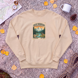 Pebble tan Rocky Mountain National Park sweatshirt with vintage elk and mountain stamp, flat-lay on granite with trail map